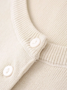 Detailed close-up of cream knit cardigan featuring ribbed crew neck and white buttons