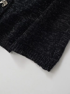 Détail du haut en maille noire avec fils argentés et bouton fleur élégant