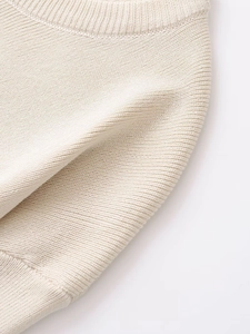 Close-up of fine plain knit texture and ribbed detailing on cream white long sleeve sweater