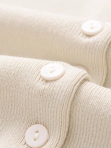 Close-up of cream knit fabric texture with vertical ribbing and matching round buttons