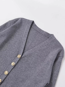 Close-up of gray knit cardigan featuring textured fabric and embossed gold buttons