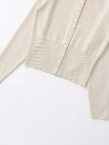 Detail of light beige knitted cardigan featuring a multi-button placket and ribbed hemline
