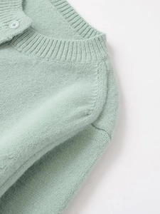 Detail of mint green knit cardigan featuring a ribbed crew neck and matching resin button