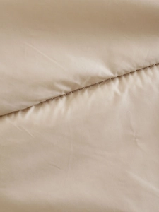 Close-up detail of quilted beige puffer vest fabric with smooth texture and stitching