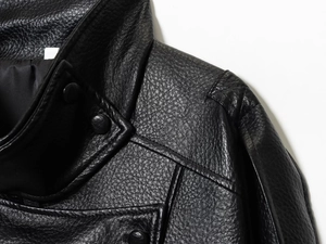 Détail macro du cuir grainé avec boutons-pression et coutures sur la veste noire