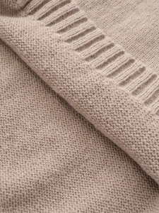 Macro detail of oatmeal knitted sweater showing ribbed cuff texture and soft fibers