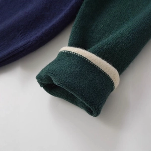 Close-up of contrast striped cuffs on a dark green minimalist long sleeve knit sweater