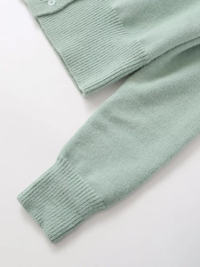 Close-up of mint green knit cardigan with ribbed cuffs and small white buttons