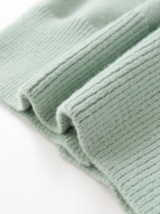 Close-up of sage green knit sweater showing ribbed cuff detail and soft fabric texture