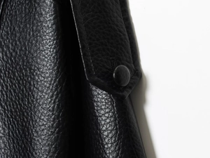 Détail d'une veste en similicuir noir montrant le grain de cuir et l'épaulette à bouton