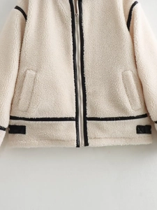 Detail of cream faux shearling jacket featuring black leather piping and silver metal zipper