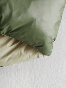 Detail of double-sided padded vest showing green and beige fabric texture and stitching
