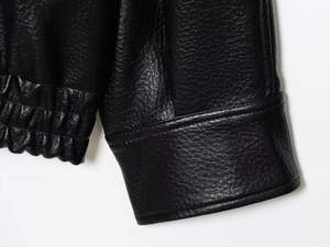 Détail de la manchette d'une veste en similicuir noir avec texture grainée et coutures