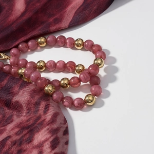 Détail d'un collier de perles bordeaux marbrées avec fermoir mousqueton doré