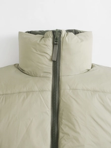Detailed close-up of light olive quilted vest collar with stand-up neck and resin zipper