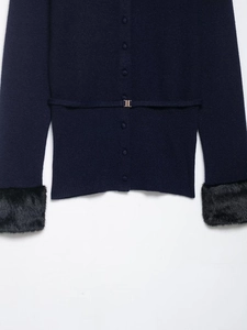 Detail of navy knit cardigan with black faux fur cuffs and a gold metal buckle belt