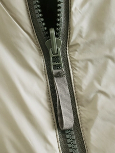 Detail of green resin zipper and beige fabric texture on the sleeveless cotton vest