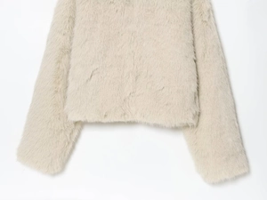 Détail de la texture douce en fausse fourrure sur l'ourlet et le poignet du manteau crème