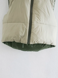 Detail of quilted vest hem featuring beige outer fabric and contrast green lining detail