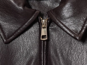 Detail shot of the dark brown faux leather texture and silver zipper on the pilot jacket