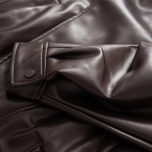 Detailed view of dark brown leather jacket sleeve with round press stud and neat stitching