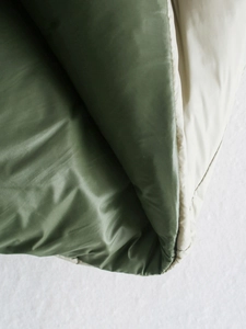 Close-up of reversible padded vest with cream exterior and olive green quilted lining