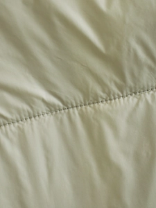 Close-up of light green quilted fabric texture and stitching details of padded vest