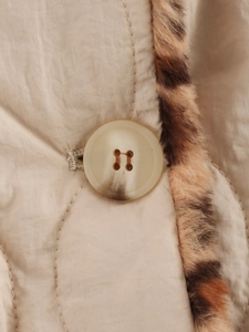 Detail of beige quilted jacket featuring leopard faux fur trim and textured button