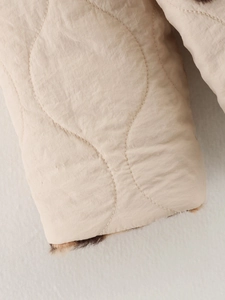 Detailed close-up of quilted beige jacket sleeve with faux fur lining and fine stitching
