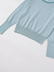 Detail view of round neckline with blue beadwork and rhinestones on a knit sweater