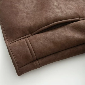 Detailed close-up of dark brown suede jacket showing precise stitching and pocket texture