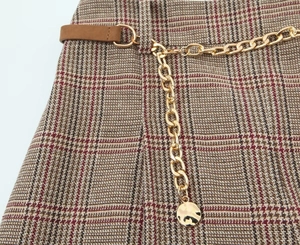 Detailed view of high-waist houndstooth shorts with gold chain and brown leather belt