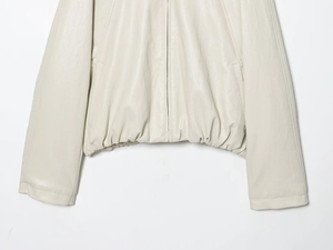 Close-up of beige faux leather bomber jacket showing elastic hem and metal zipper detail