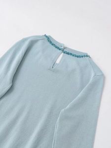 Detail of light blue knit top featuring beaded neckline and teardrop back cutout