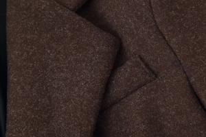 Macro shot of dark brown wool coat showing premium fabric texture and pocket stitching details