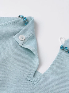 Detail of light blue knit sweater featuring ornate blue rhinestone flower embellishments