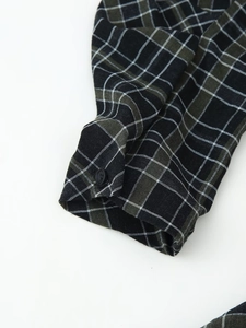 Détail de la manchette d'une robe à carreaux noirs et verts avec bouton mat