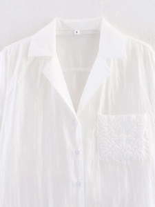 Detailed close-up of white long sleeve shirt with floral embroidery on the pocket