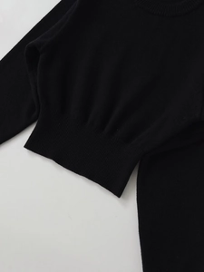 Détail du pull en maille noire montrant les poignets côtelés et la texture du tissu