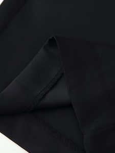 Close-up of black satin fabric showing fine overlock stitching and hem detail on trousers