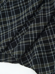 Détail rapproché du tissu à carreaux montrant la texture et les plis noirs et olive