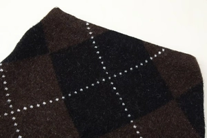 Close-up of knit fabric showing brown and black argyle pattern with fine white stitching