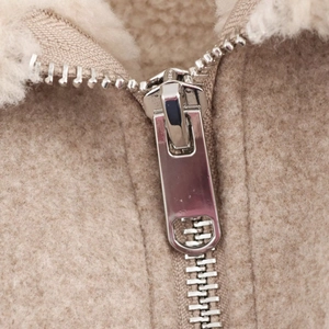 Dettaglio della cerniera in metallo e della trama pelosa su questa giacca in pile beige