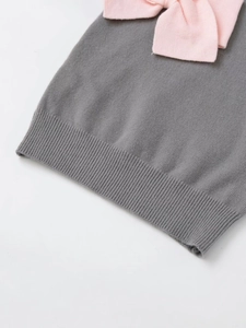 Detail of grey knitted vest featuring a pink contrast bow and ribbed hem texture