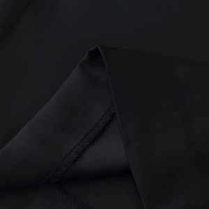 Macro shot of black satin pants showing delicate texture and fine overlock stitching