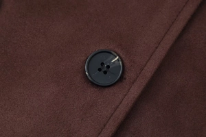 Macro detail of dark brown wool coat fabric with a polished amber marble button
