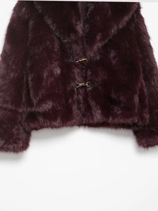Detail of burgundy faux fur coat with golden metal buckles and plush texture