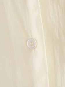 Macro shot of durable four-hole white button on smooth beige silk shirt fabric