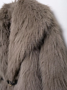 Detail shot of long faux fur coat texture with black leather strap and gold buckle