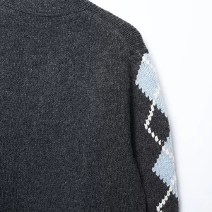 Macro shot of dark grey knit cardigan showing argyle pattern on sleeve detail